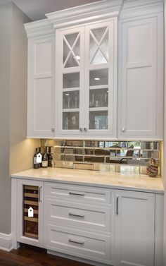 a kitchen with white cabinetry and marble counter tops, along with wine bottles in the bottom drawer