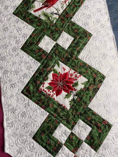 a quilted table runner with poinsettis and holly leaves on the border