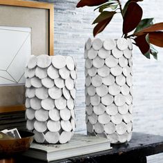 two white vases sitting on top of a table next to a potted plant