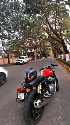 a red and black motorcycle parked on the side of a road next to a white car