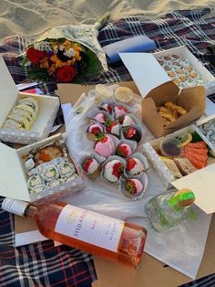 an assortment of sushi and other foods on a picnic blanket with wine, water bottle, and flowers