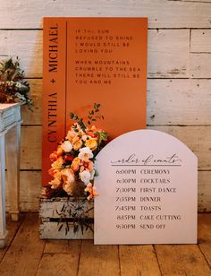 an orange and white wedding sign next to a bouquet of flowers on a wooden floor