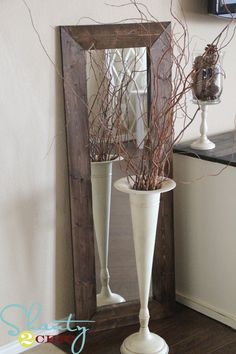 a mirror and some branches in a vase on the floor next to a table with a vase