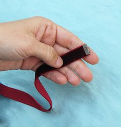 a hand holding a red ribbon on top of a blue surface with scissors in it