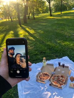 a person taking a photo of two pizzas on a picnic blanket with the sun behind them