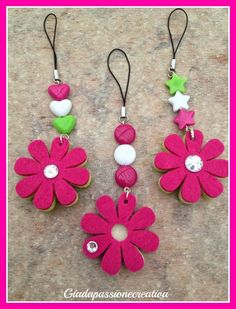 three pink flowers with green leaves and white hearts hanging from earwires on a stone surface