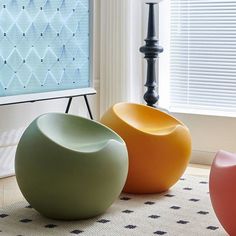 three different colored chairs sitting in front of a flat screen tv on a stand next to a window