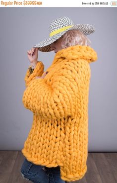 a woman in a yellow sweater and hat is standing on the floor with her hands behind her head