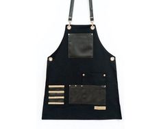 a black apron with gold trimmings and two pockets on the front, hanging from a hook