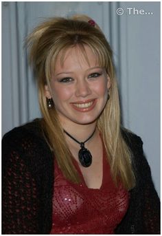 a woman with long blonde hair wearing a red top and black cardigan smiling at the camera