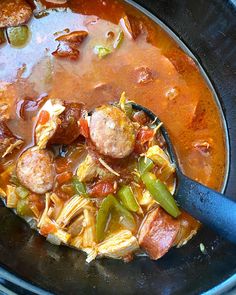 a spoon full of soup with meatballs, peppers and noodles on the side in a black bowl