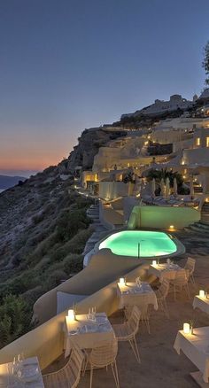 an outdoor dining area overlooking the ocean at dusk with lit tables and chairs on the beach