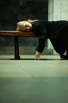 a woman laying on top of a wooden bench with her head down and hands in the air