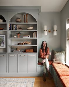 a woman sitting on a bench in front of a bookshelf filled with shelves