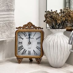 a clock sitting on top of a bathroom counter next to a vase filled with flowers