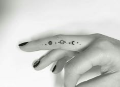 a woman's hand with a small tattoo on the middle finger, and planets