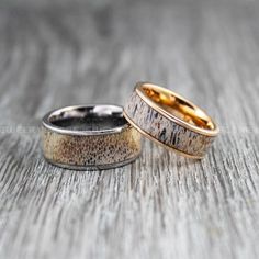 two gold wedding bands with black speckles are on a wooden surface and one has an antler ring in it's center