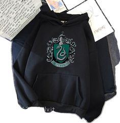 a harry potter hoodie with the sly crest on it, next to an open book