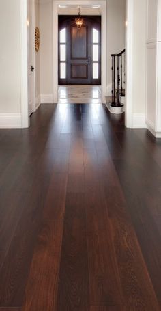 an empty hallway with wooden floors and white walls, leading to a front door that leads into another room