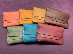 four different colored leather wallets sitting next to each other on a purple cloth background