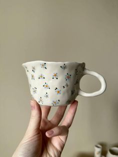 a hand holding up a white cup with flowers on it