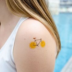 a woman with a yellow bicycle tattoo on her left upper arm and shoulder, next to a swimming pool