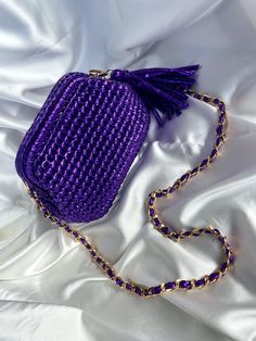 a purple purse sitting on top of a white bed next to a gold chain strap