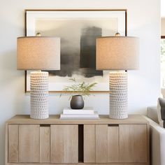 two lamps sitting on top of a wooden cabinet in a living room next to a couch