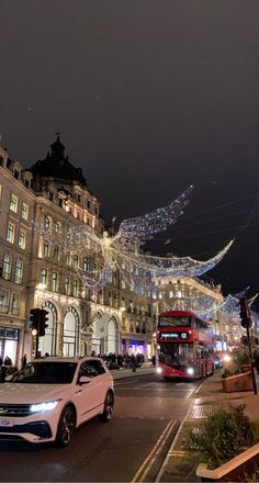 a white car driving down a street next to tall buildings with christmas lights on them