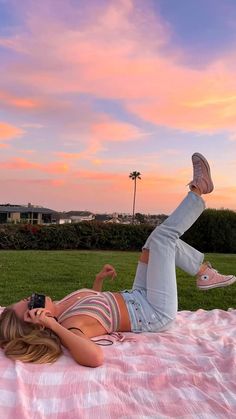 a woman laying on top of a pink and white blanket next to a green field