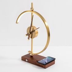 a clock with a cell phone on it sitting in front of the clock face and base