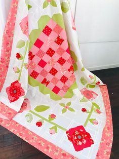 a pink and green quilted blanket sitting on top of a wooden floor next to a white door