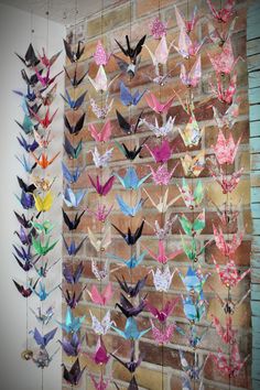 several colorful origami birds hanging from strings on a brick wall