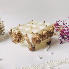 a white cake with gold decorations on it sitting next to some purple flowers and lace