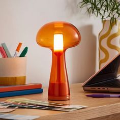 an orange table lamp sitting on top of a wooden desk next to a laptop computer