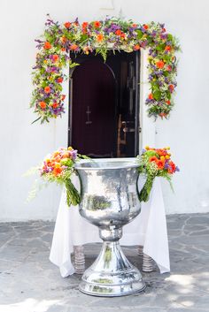 a large silver vase with flowers on it sitting in front of a door and window