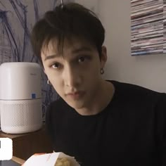 a young man sitting at a table with food in front of him and an air freshener on the wall behind him