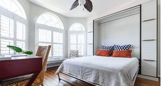 a bed sitting in a bedroom next to two windows with shutters on each side