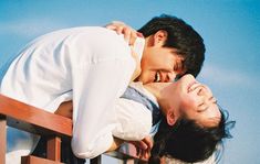 a man and woman standing next to each other on top of a wooden bench with blue sky in the background