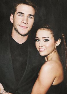 a young man and woman posing for a photo in front of a black background, with one smiling at the camera