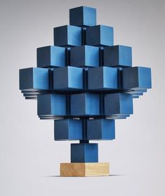 a blue sculpture made out of cubes sitting on top of a wooden block in front of a white wall