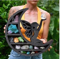 a woman holding up a wooden sculpture with crystals and a butterfly on it's back