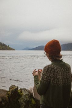 a woman standing on top of a rocky beach next to the ocean