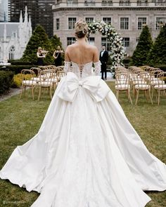 a woman in a wedding dress standing on the grass with her back to the camera