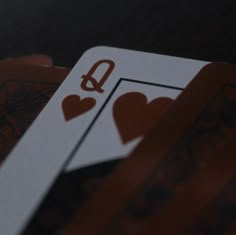 two playing cards with hearts on them sitting next to each other in front of a dark background