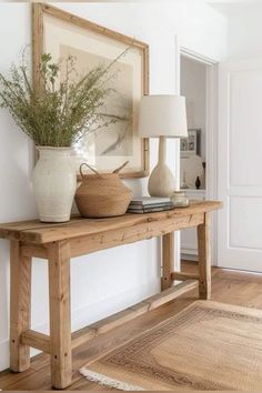 a wooden table with two vases and a lamp on it in front of a white wall