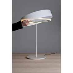 a person is holding the light on top of a white table lamp with a circular base