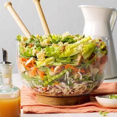 a salad with carrots, lettuce and chicken in a glass bowl next to a bottle of orange juice