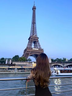 a woman standing in front of the eiffel tower looking out over the water