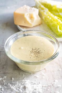 a glass bowl filled with dressing next to lettuce and cheese on a table